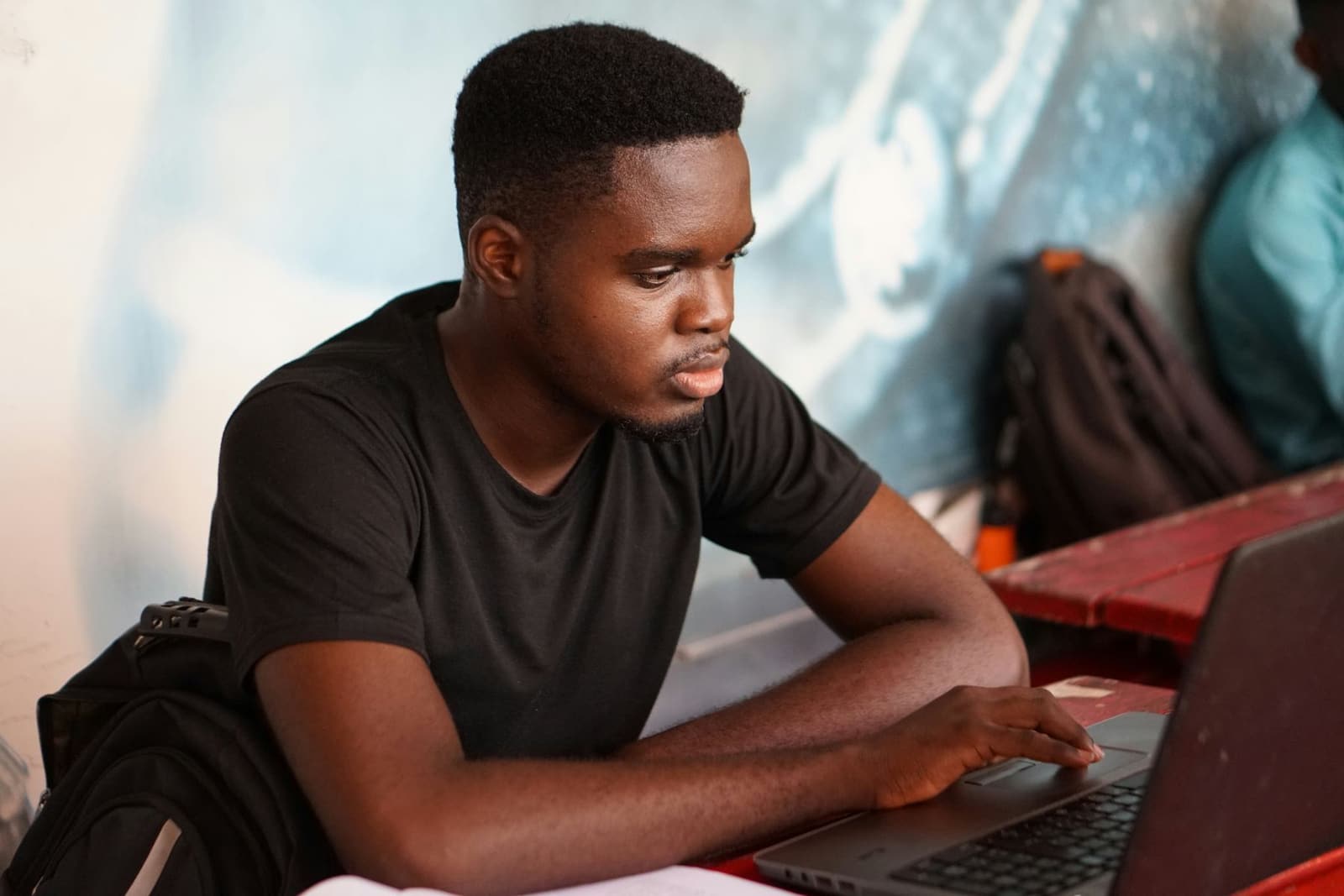 A young Black man in a black T-shirt reading carefully on his laptop