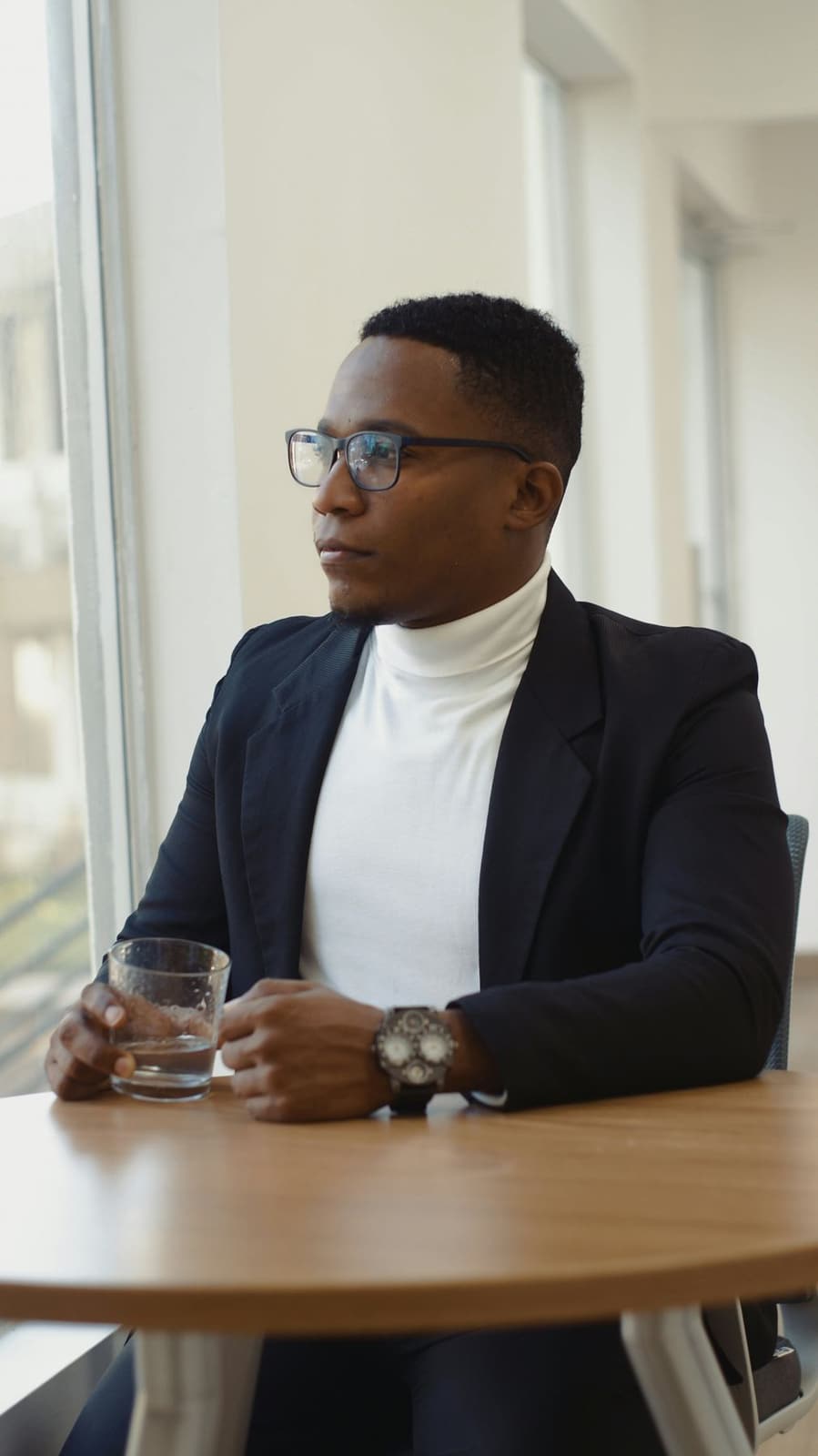 A Black man in a dark suit sitting at a table, looking composed and prepared